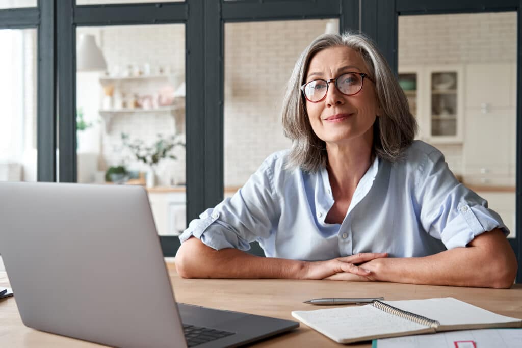 En kvinde med briller sidder ved et skrivebord og er optaget af sin laptop