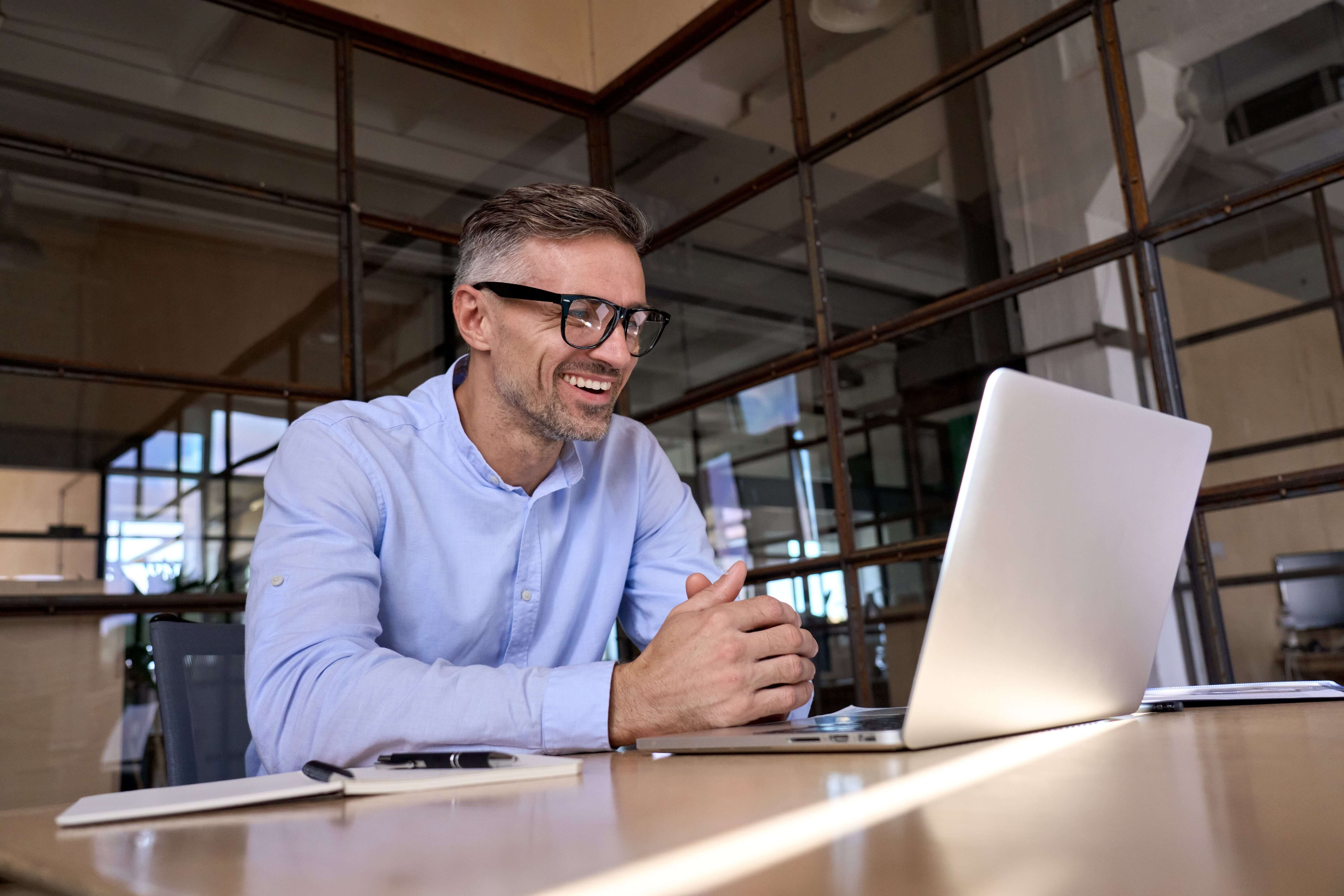 En mand med briller smiler, mens han arbejder på sin bærbare computer