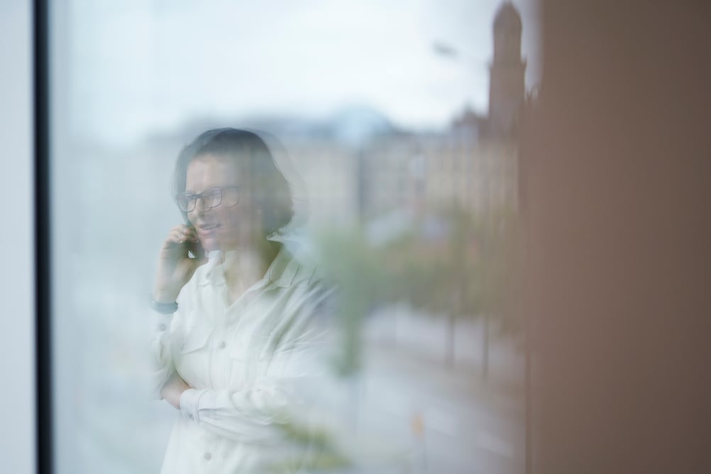 A woman in a white shirt speaks on the phone while looking out of a window