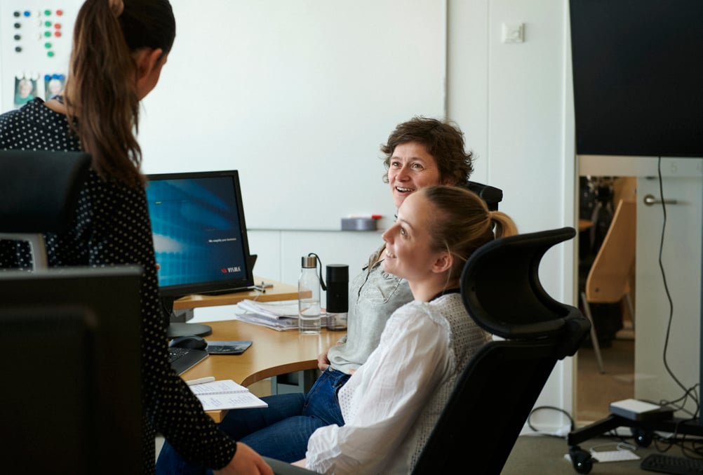 Three women sit and chat around a desk