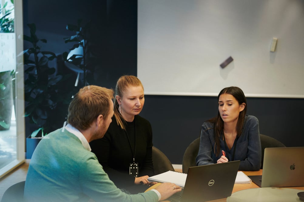 Three coworkers sit around a table discussing next steps on a project