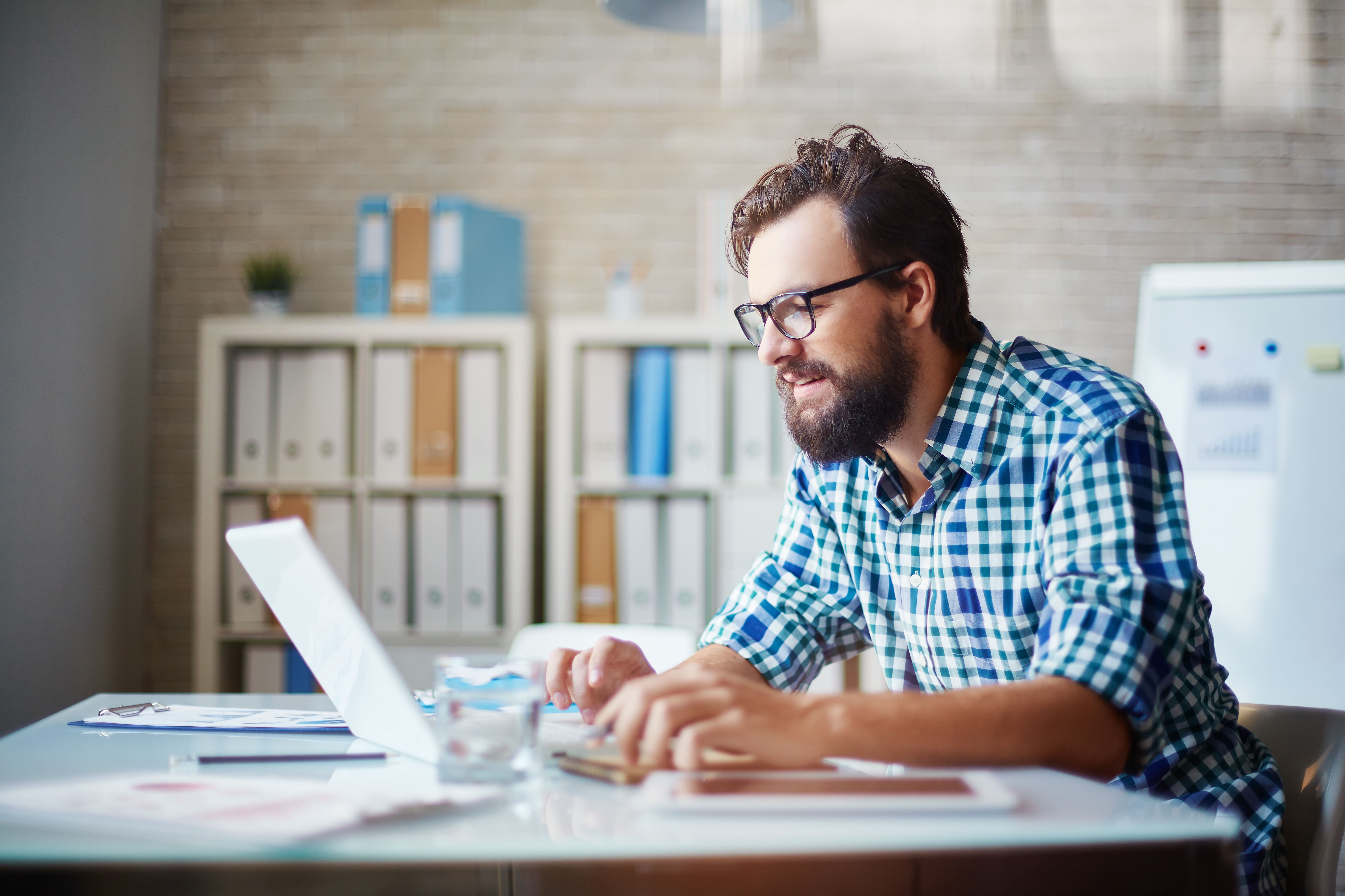 A man is typing on a laptop in a bright, modern office.