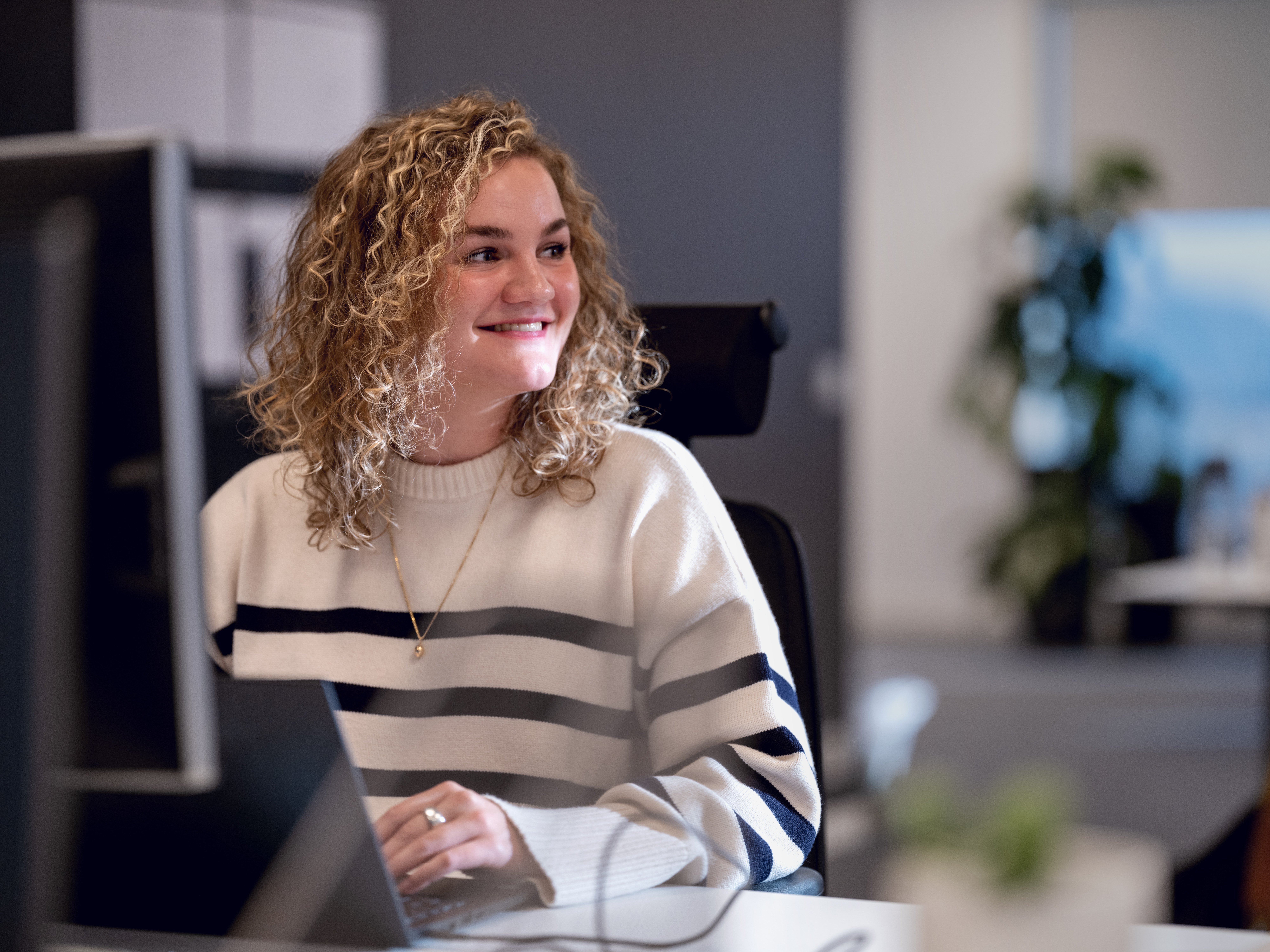 En kvinde iført en stribet sweater smiler, mens hun bruger sin computer.
