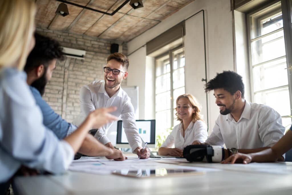 Man in glasses is explaining something to a woman across a conference table in an office with city views.