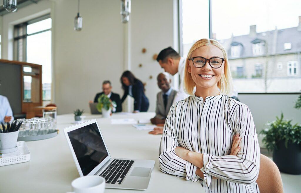 Smiling woman with glasses using a laptop at a table.