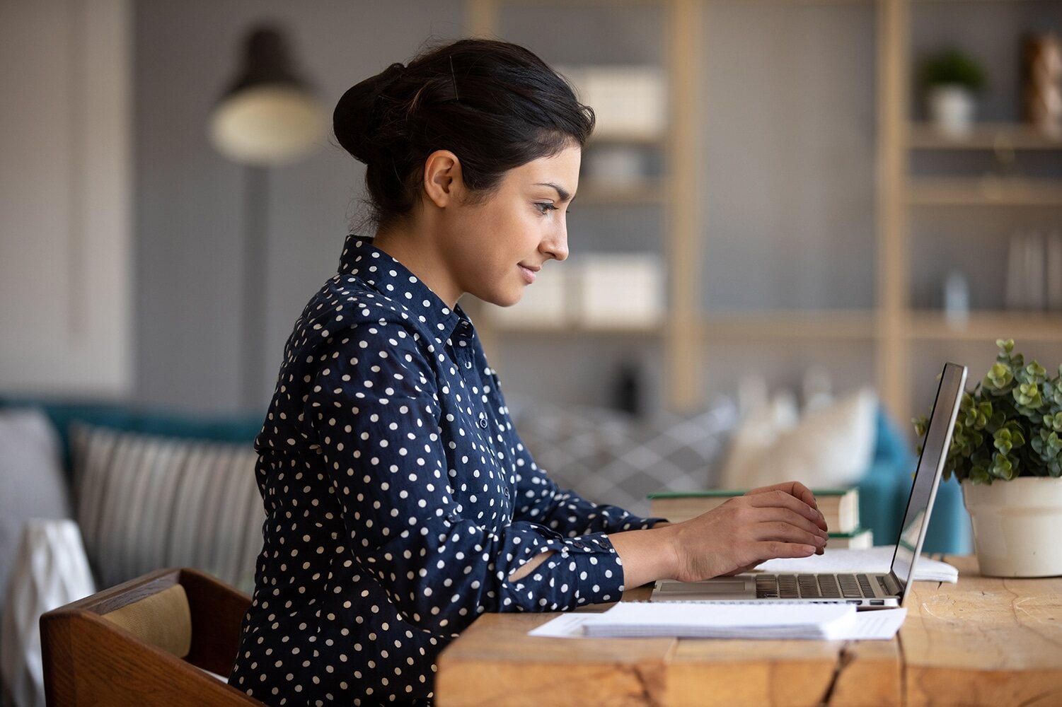 A woman sitting at a table with a laptop, concentrating on her work