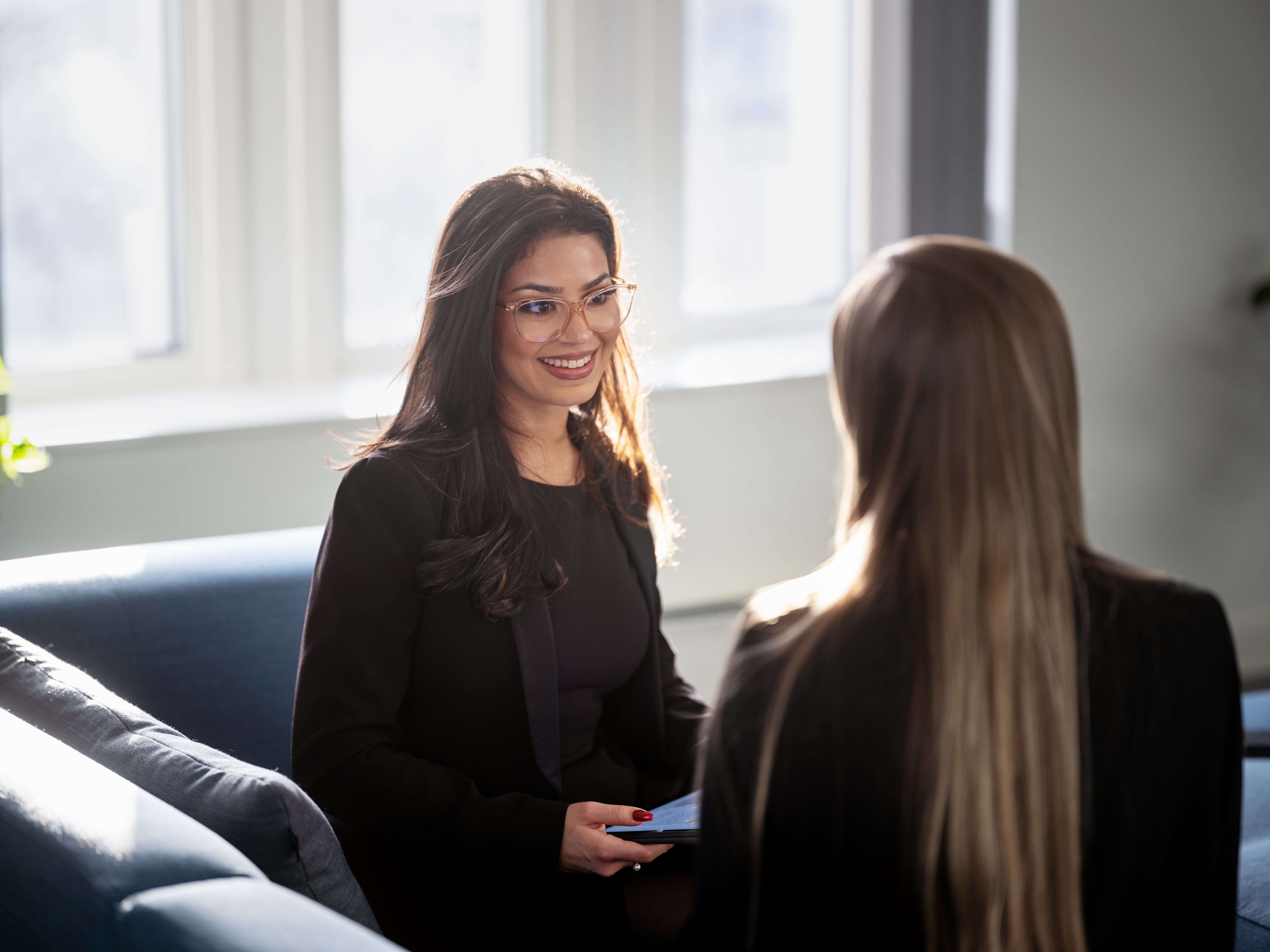 Two colleagues chatting while sitting on a couch in a modern office setting.