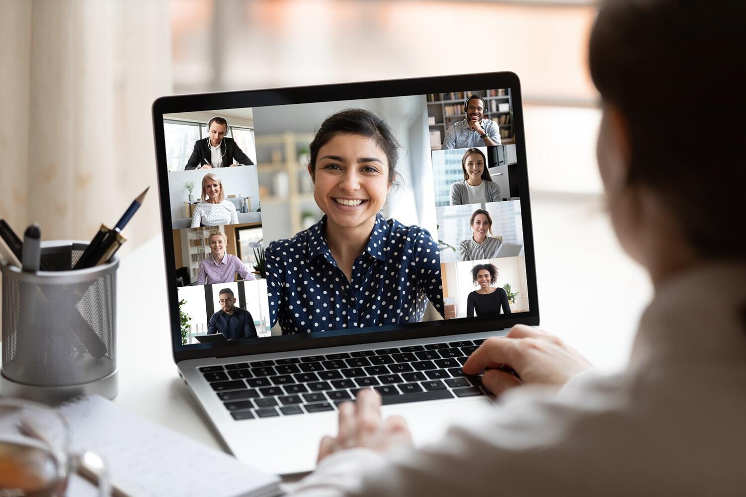 A woman engaged in a video call on her laptop, with multiple participants visible on the screen.