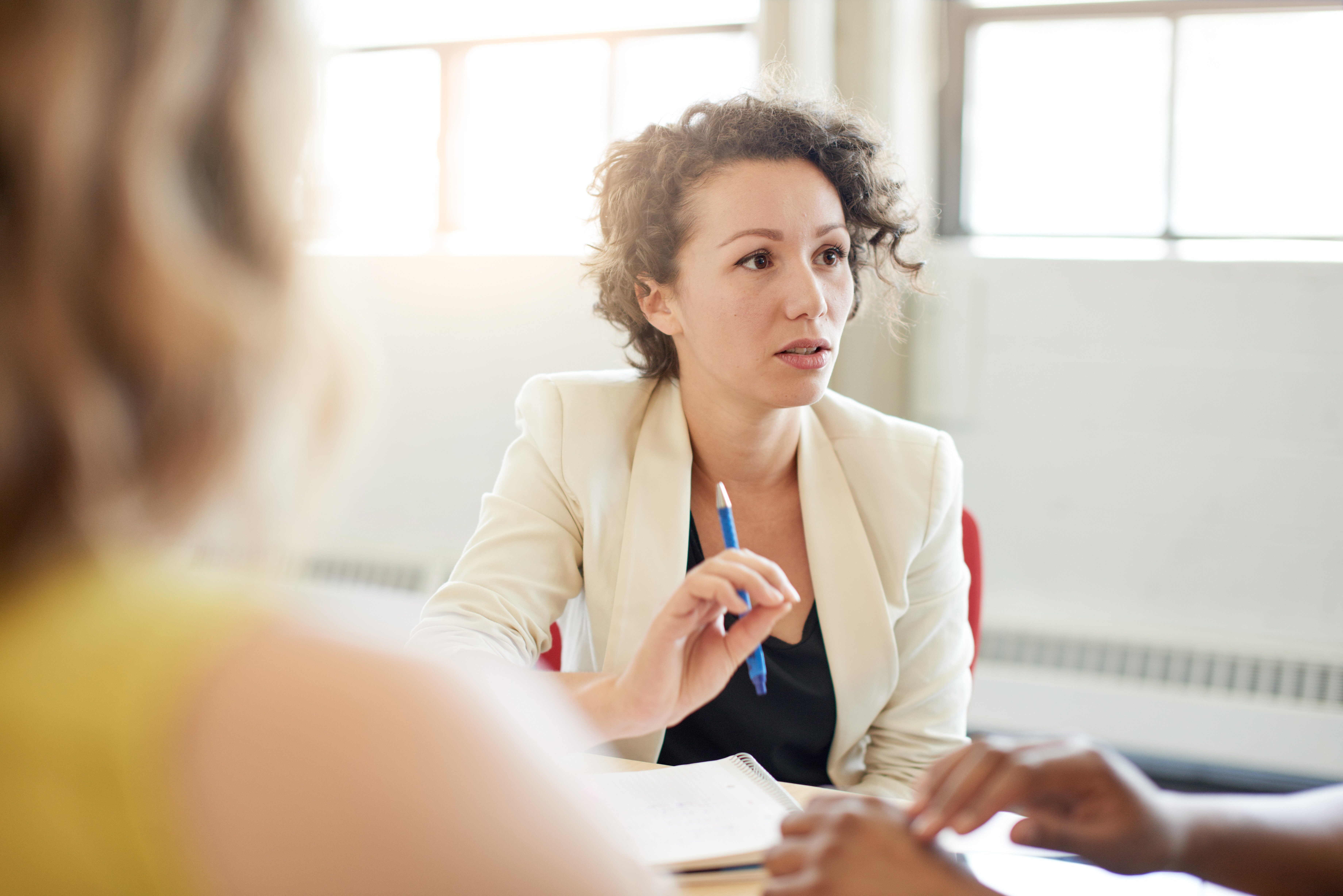 A woman speaking at a meeting while holding a pen.