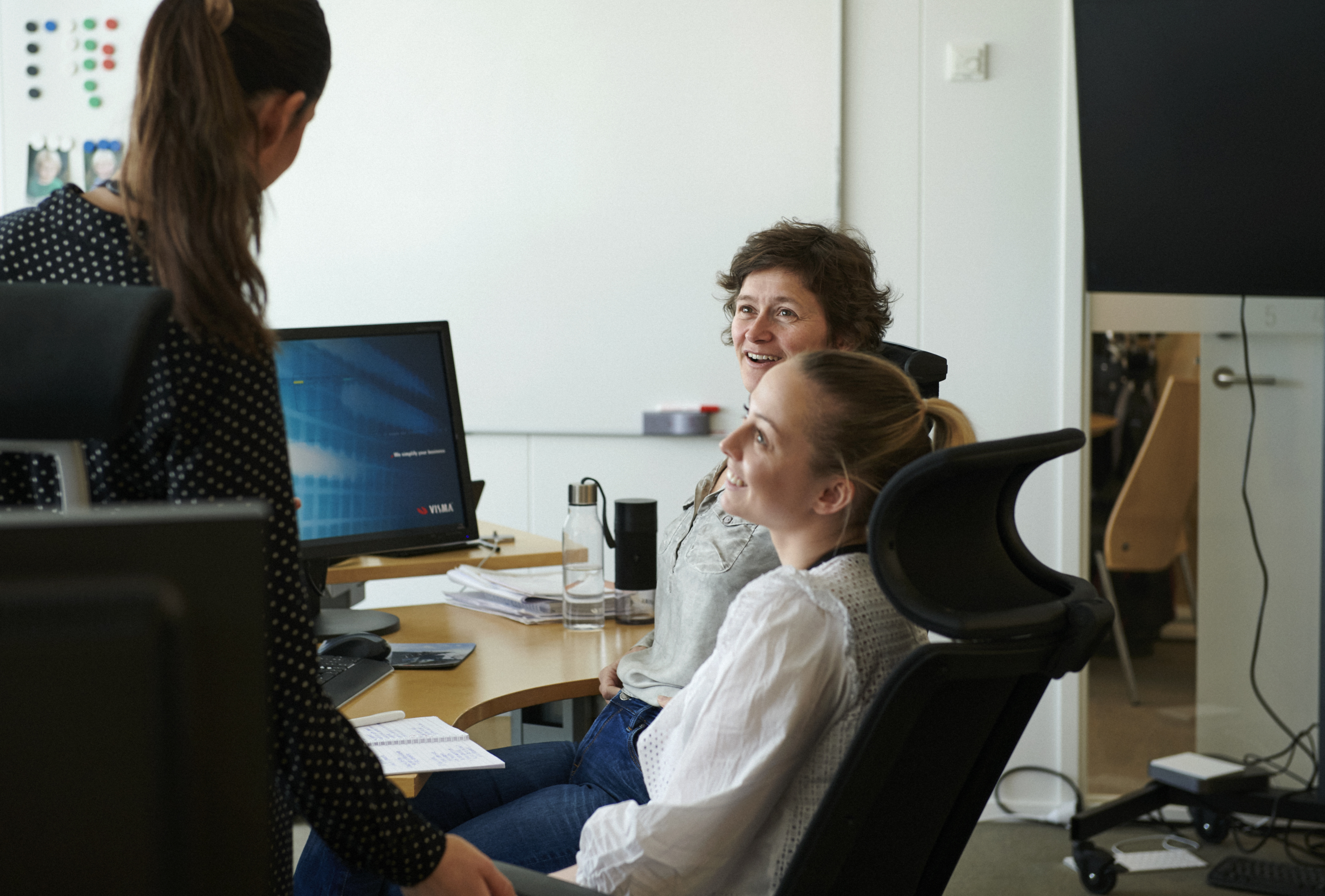 Man in glasses is explaining something to a woman across a conference table in a high-rise office with city views.