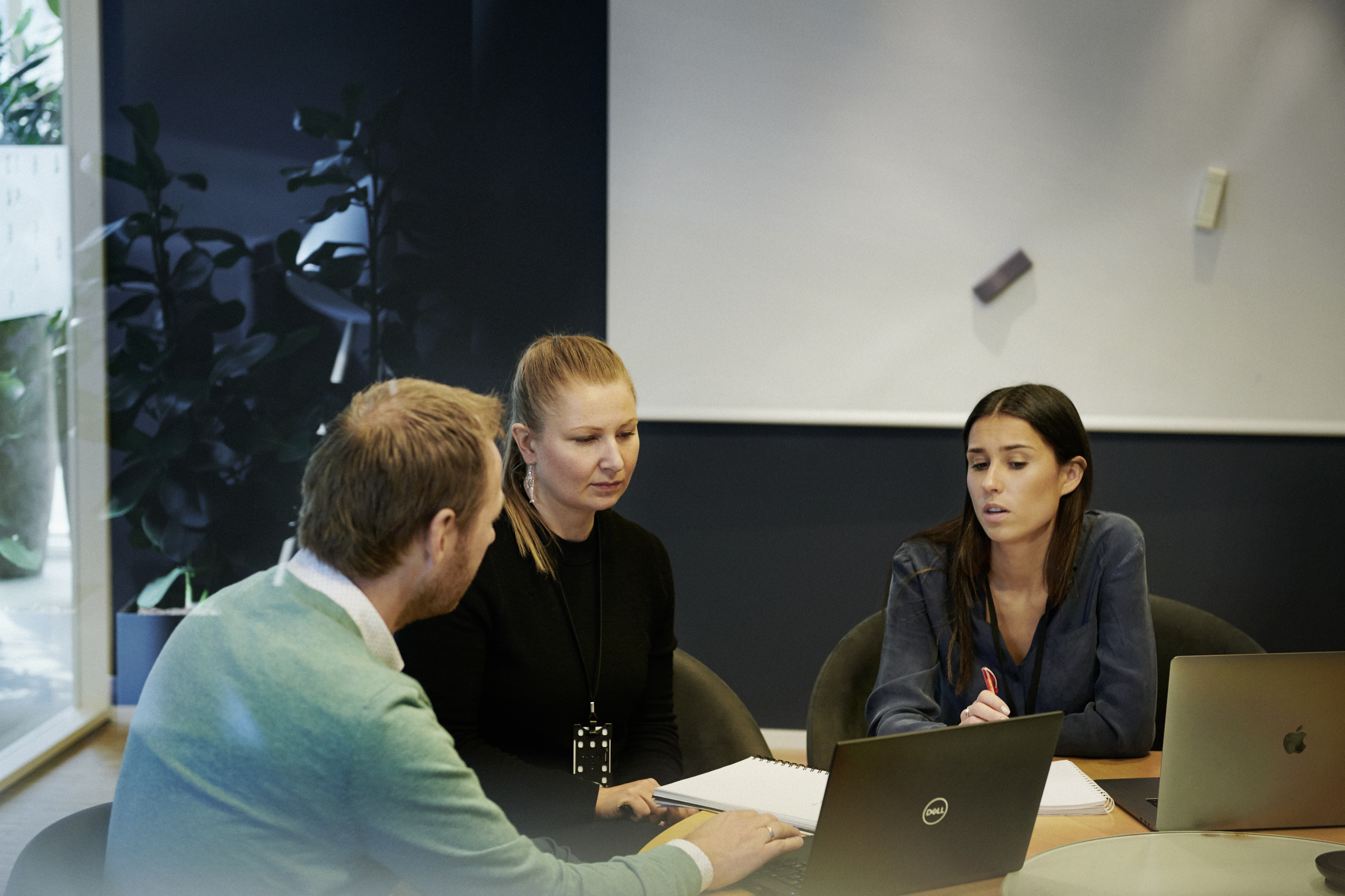 Three employees seated at a table in an office during a meeting.